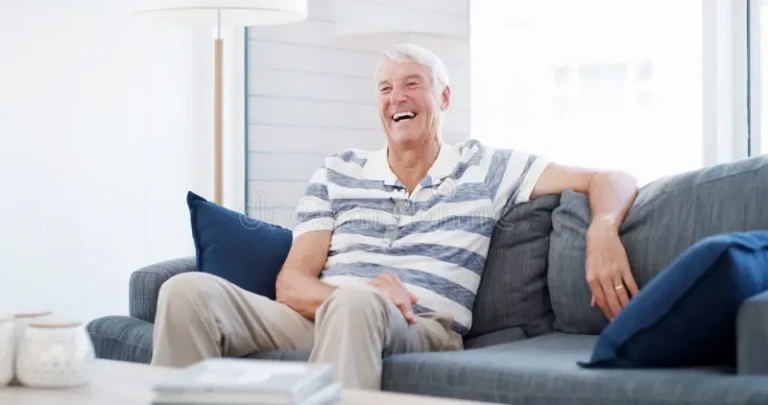 senior-man-laughing-watching-tv-sofa-streaming-relax-funny-movie-lounge-retirement-elderly-person-smile-368781603